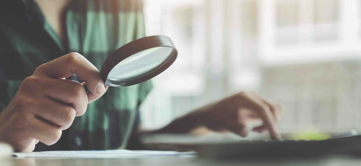 Business man using magnifying to review balance sheet annual with using laptop computer to calculating budget. audit and Check integrity before investment concept.