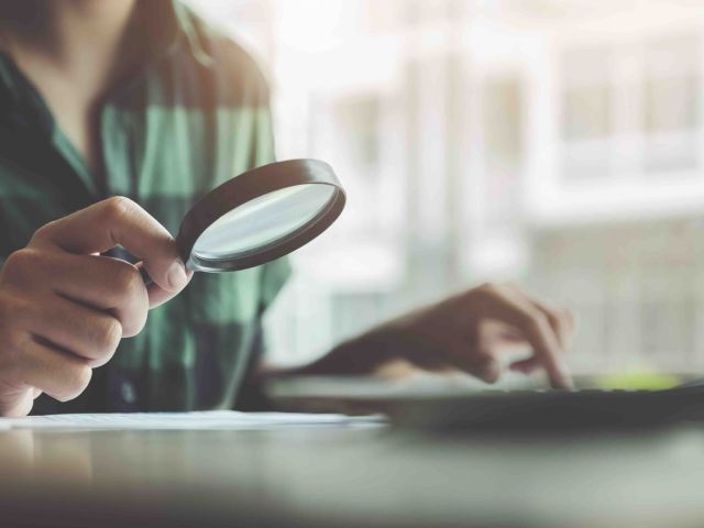 Business man using magnifying to review balance sheet annual with using laptop computer to calculating budget. audit and Check integrity before investment concept.